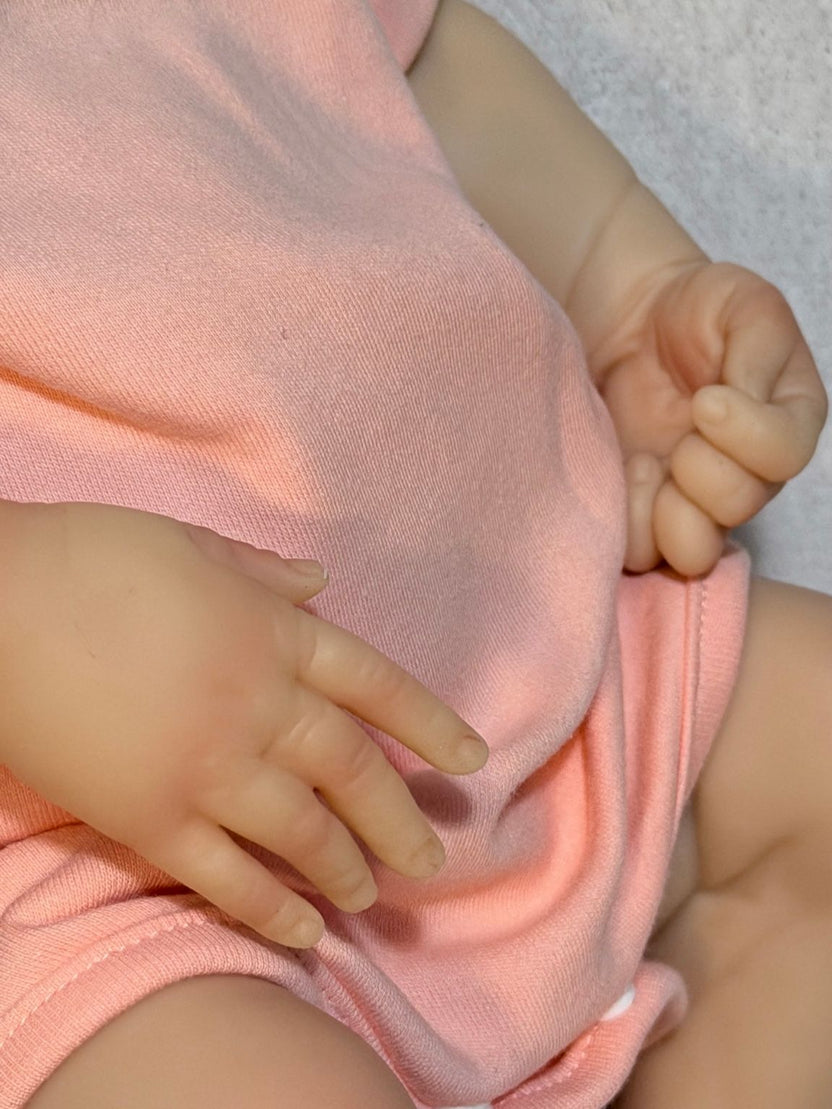Reborn bebé completa con ropa rosa y pose natural sobre fondo blanco.