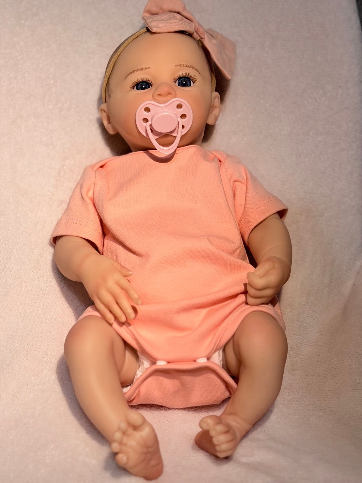 Reborn bebé fotográfica en catálogo con ropa rosa y detalles realistas