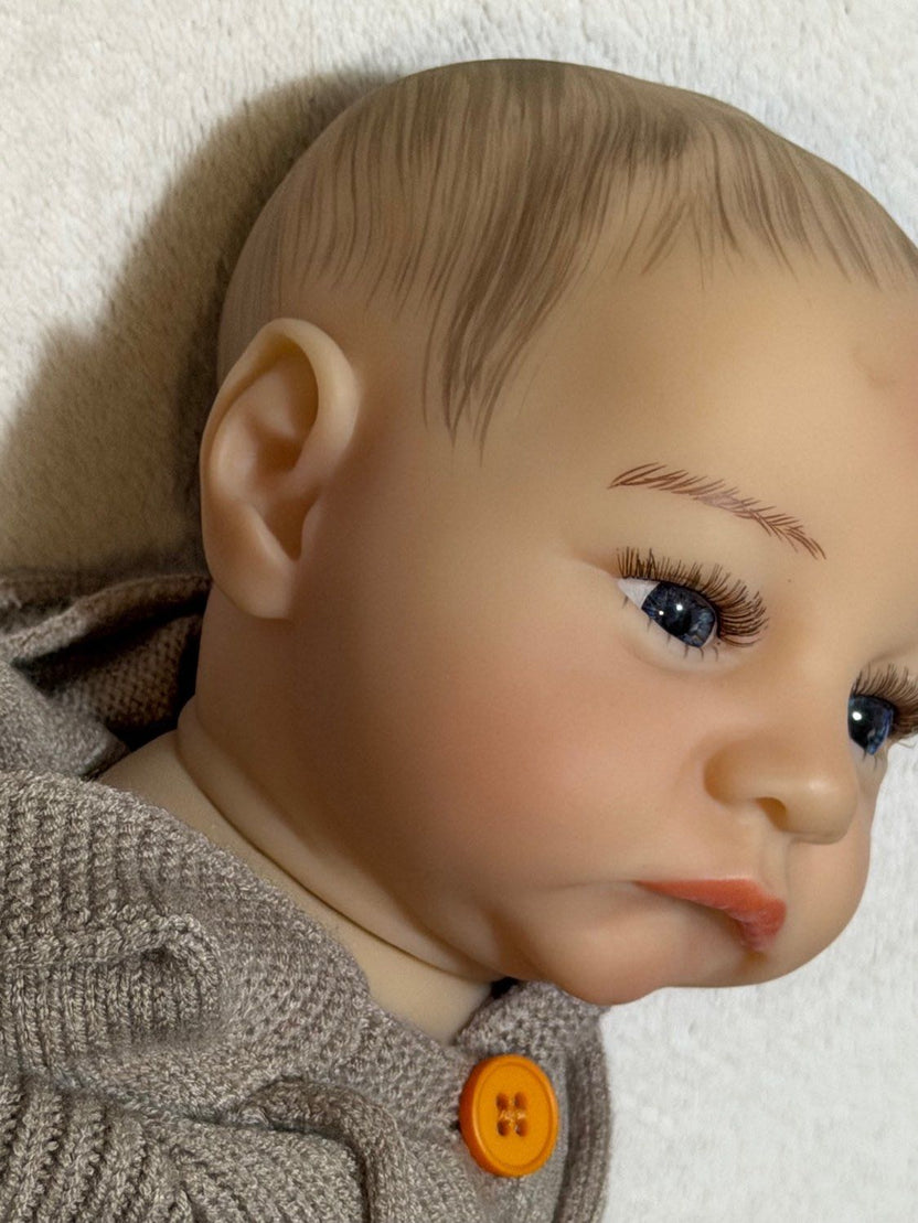 bebe reborn con vista lateral de su oreja y diseño pintado de pelo y cejas